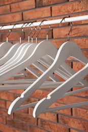 Photo of White clothes hangers on rail near red brick wall, closeup