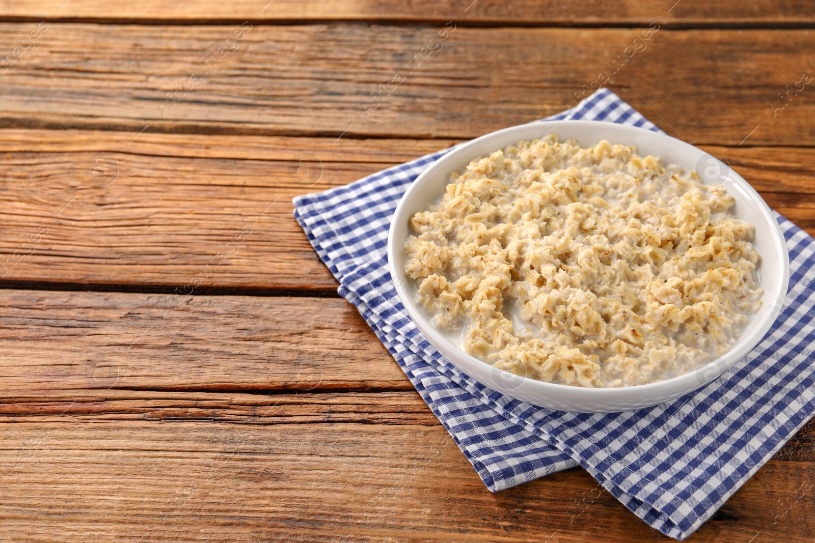 Photo of Tasty boiled oatmeal in bowl on wooden table. Space for text