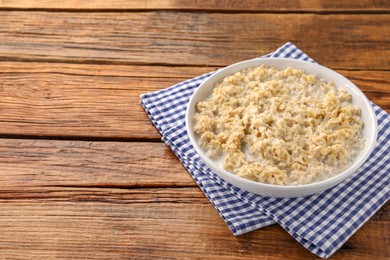 Tasty boiled oatmeal in bowl on wooden table. Space for text