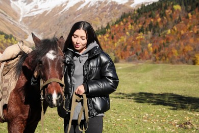 Young woman with horse in mountains on sunny day, space for text. Beautiful pet