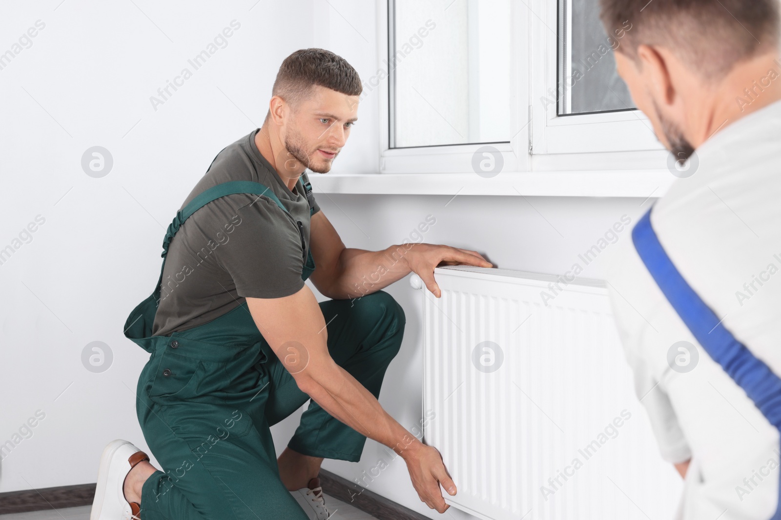 Photo of Professional plumbers installing new heating radiator in room