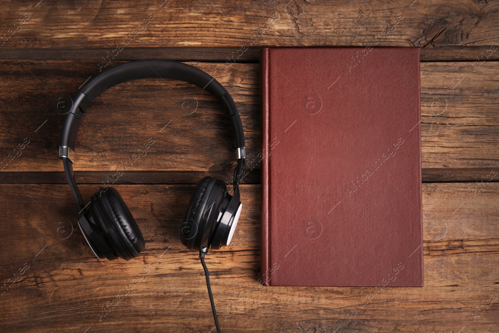 Photo of Book and modern headphones on wooden table, flat lay