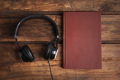 Photo of Book and modern headphones on wooden table, flat lay