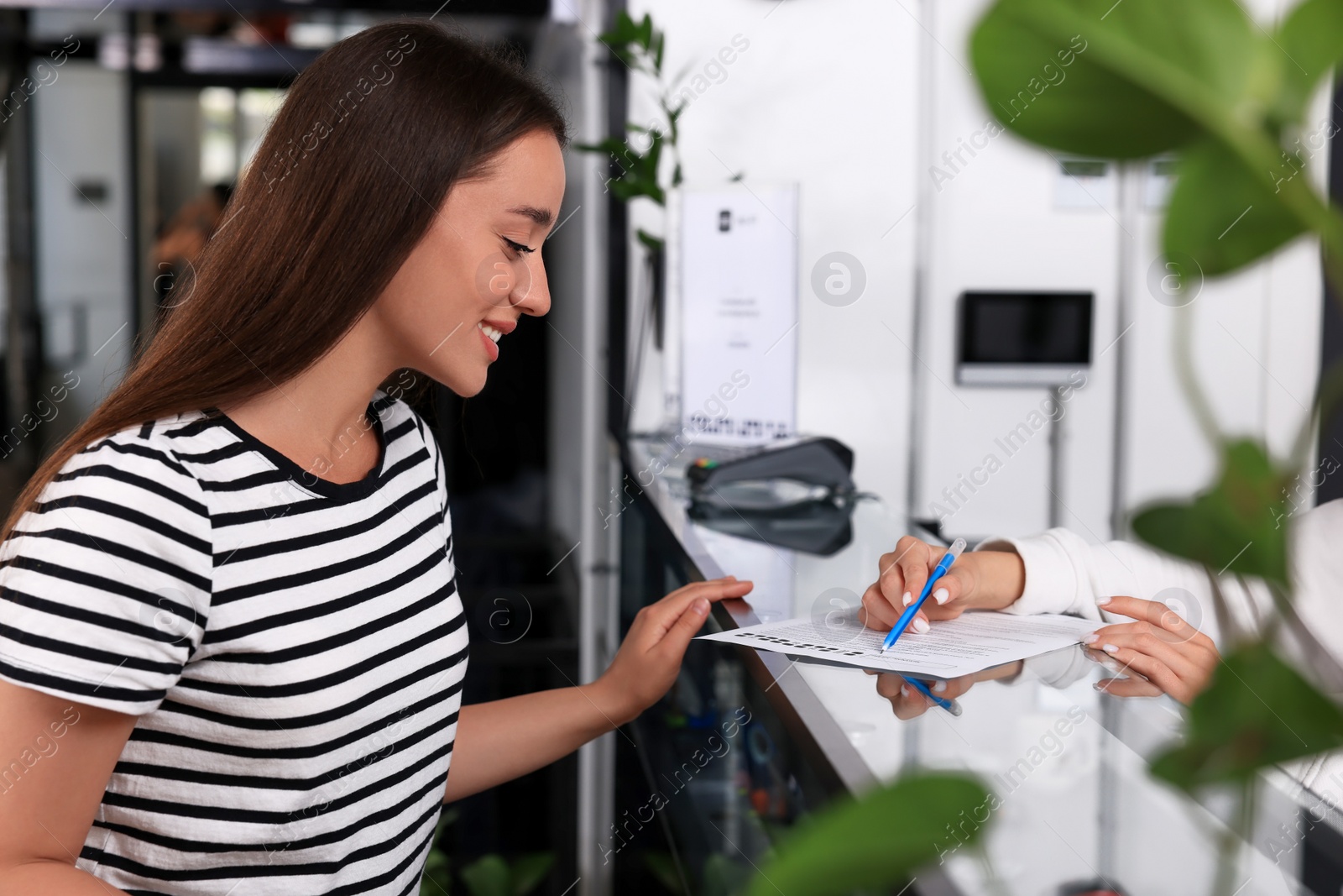 Photo of Happy young woman registering at reception desk in hostel