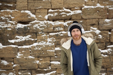 Photo of Young man listening to music with headphones against stone wall. Space for text