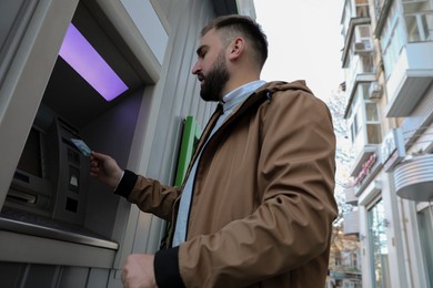 Photo of Man inserting credit card into cash machine outdoors, low angle view