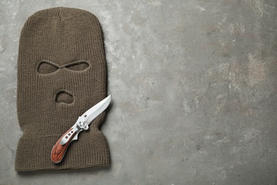 Photo of Beige knitted balaclava and knife on grey table, top view. Space for text