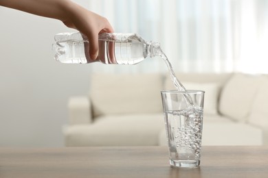 Photo of Woman pouring water from bottle into glass at table indoors, closeup