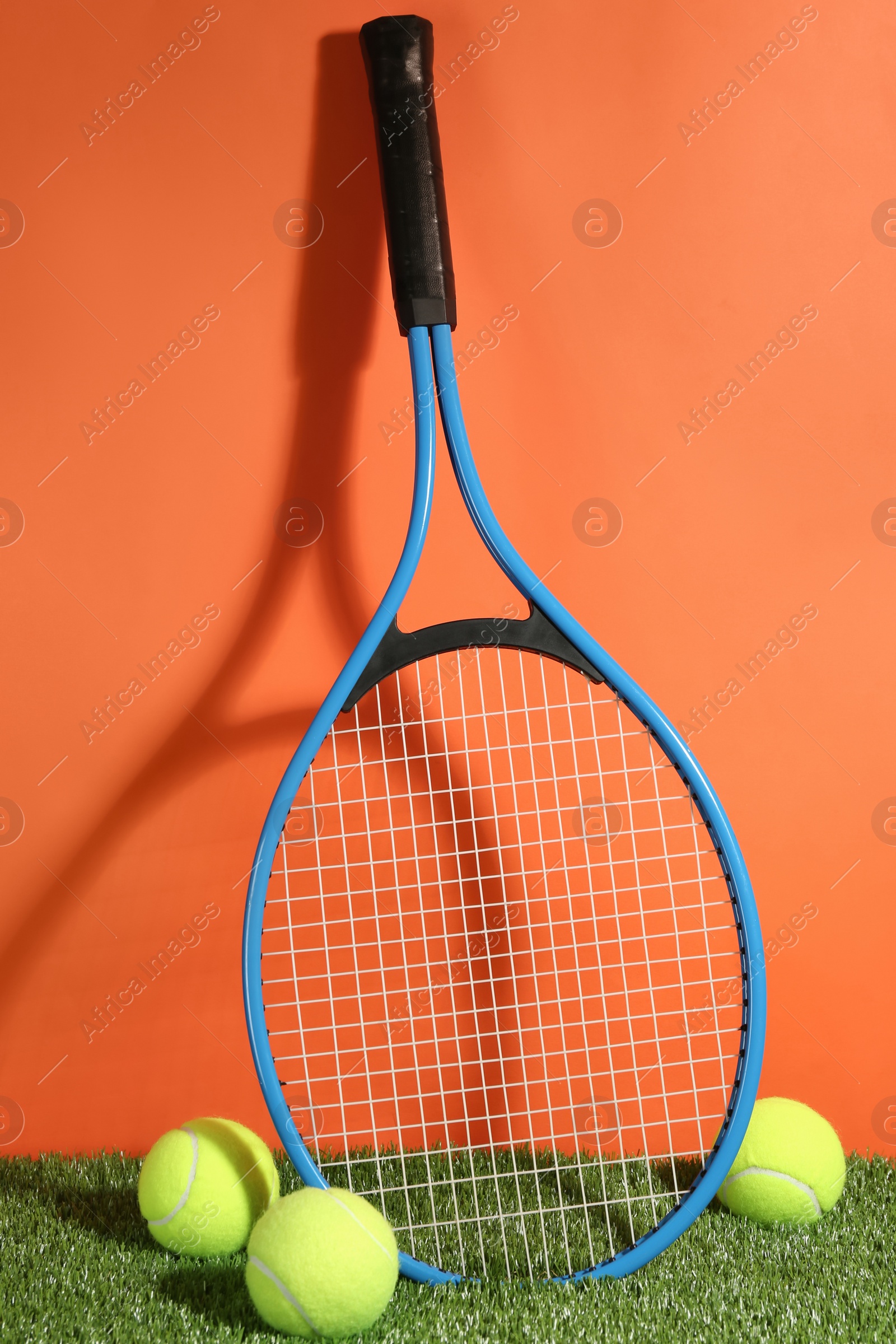 Photo of Tennis racket and balls on green grass against orange background. Sports equipment