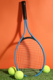 Photo of Tennis racket and balls on green grass against orange background. Sports equipment