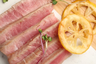 Pieces of delicious tuna steak with microgreens and lemon on serving board, closeup