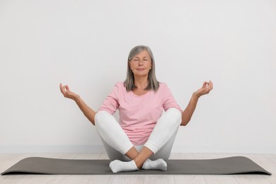 Photo of Senior woman practicing yoga on mat near white wall