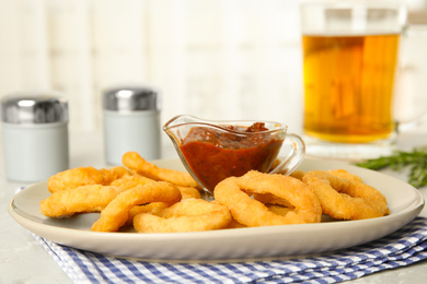 Photo of Delicious crunchy fried onion rings and sauce on grey marble table