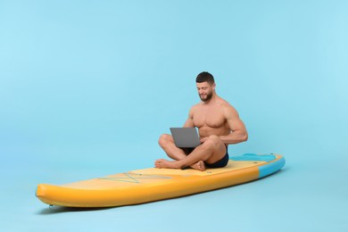 Photo of Man with laptop on SUP board against light blue background