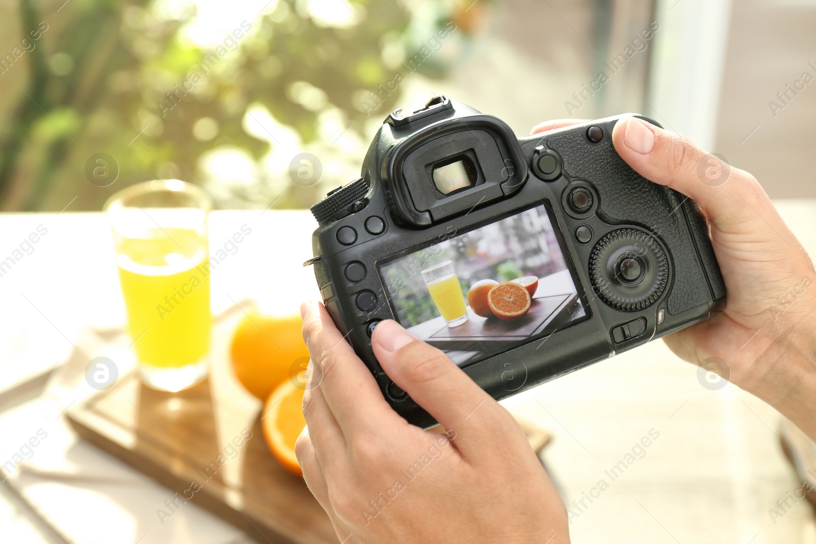 Photo of Female photographer taking picture of juice and oranges with professional camera, closeup