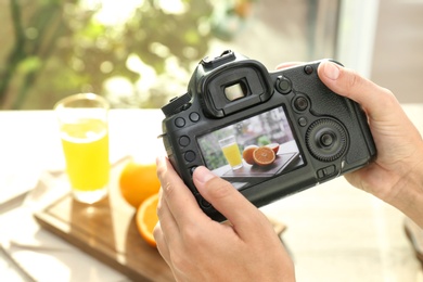 Female photographer taking picture of juice and oranges with professional camera, closeup