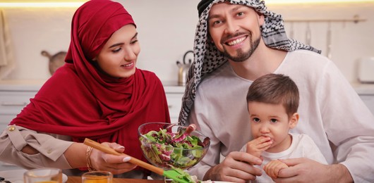 Happy Muslim family eating together at table in kitchen. Banner design