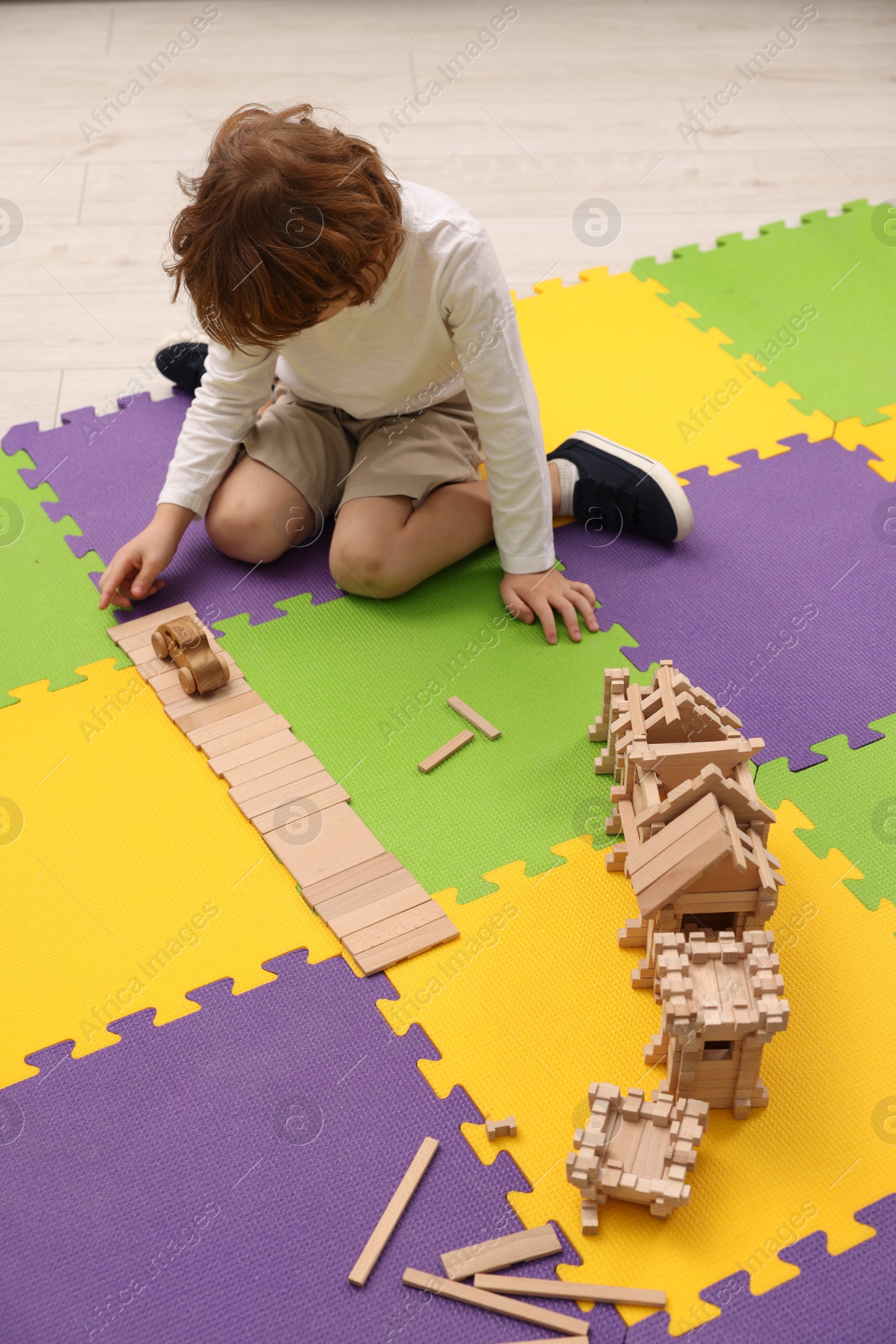 Photo of Little boy playing with wooden construction set on puzzle mat in room. Child's toy