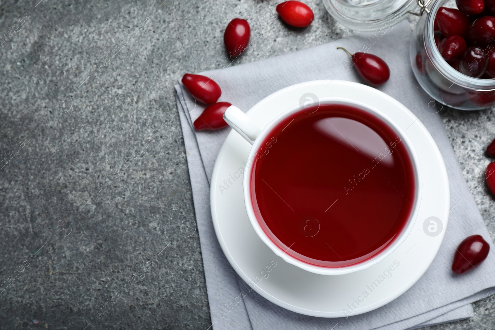 Photo of Cup of fresh dogwood tea and berries on grey table, flat lay. Space for text