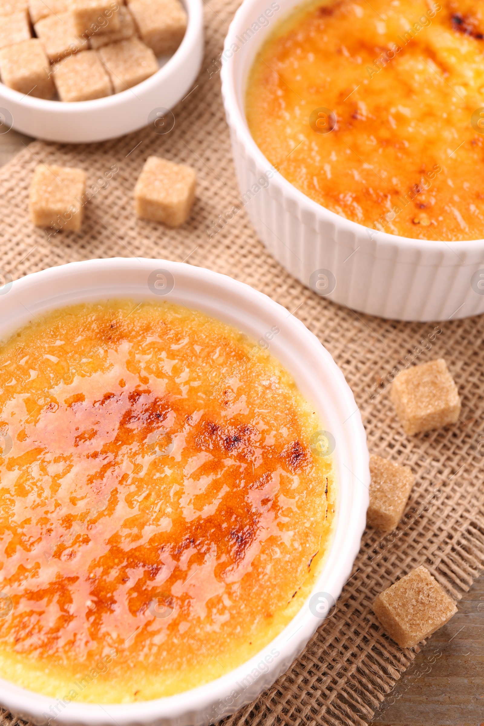 Photo of Delicious creme brulee in bowls and sugar cubes on table, above view