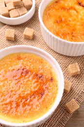 Delicious creme brulee in bowls and sugar cubes on table, above view