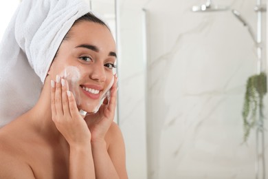 Photo of Beautiful young woman applying cleansing foam onto face in bathroom, space for text. Skin care cosmetic