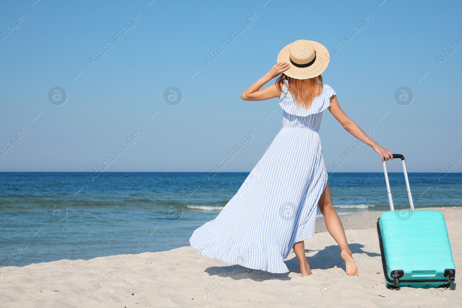 Photo of Woman with suitcase on sandy beach near sea, back view