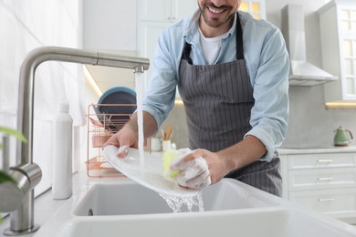 Photo of Man washing plate above sink in kitchen, closeup