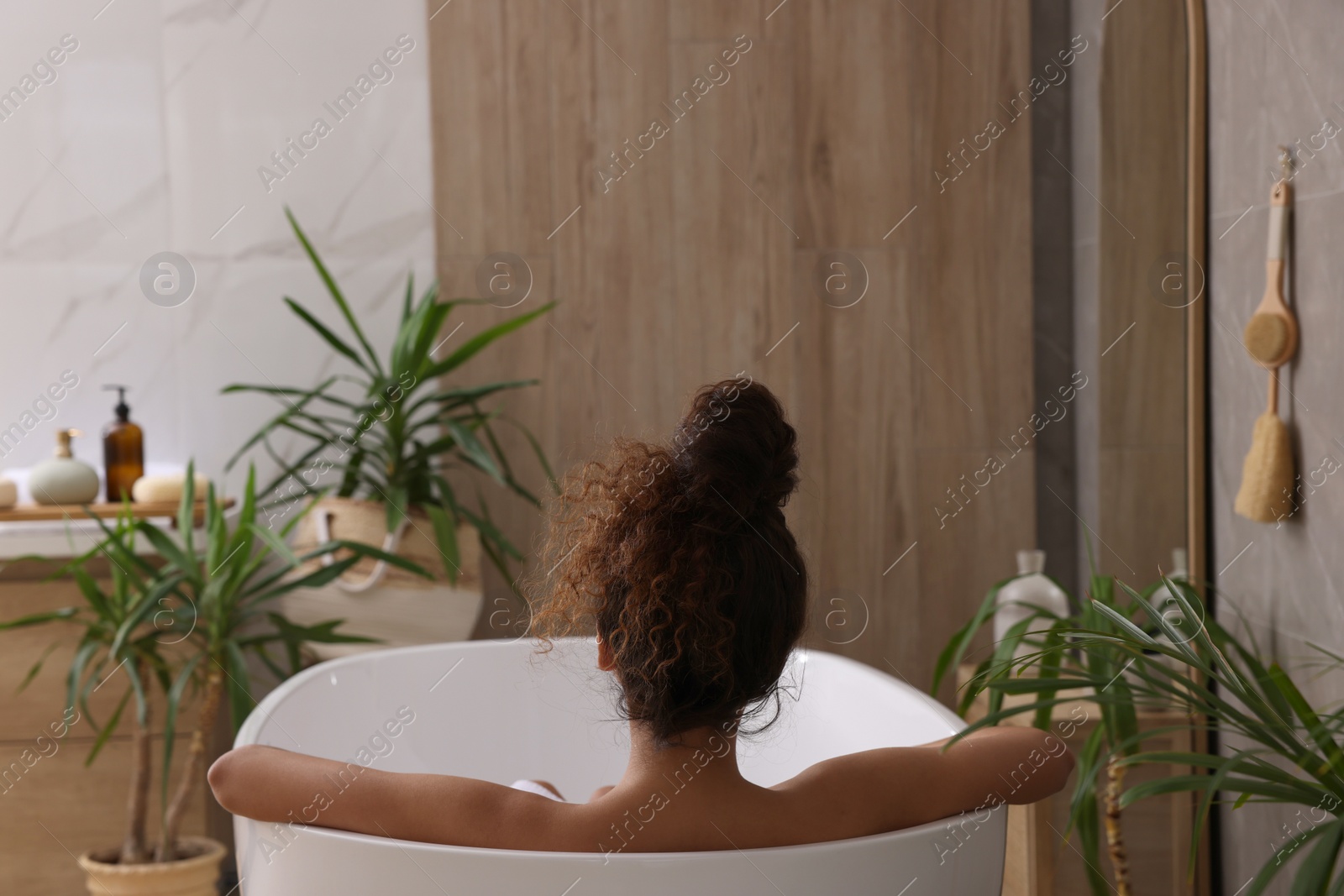 Photo of African American woman taking bath indoors, back view