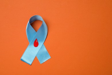 Photo of Light blue ribbon with paper blood drop on orange background, top view and space for text. Diabetes awareness