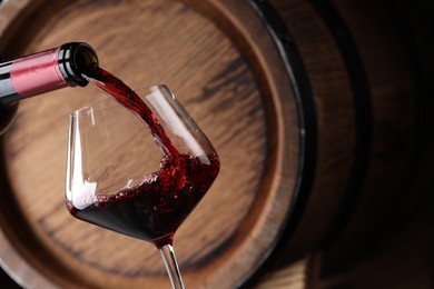 Pouring delicious wine into glass against wooden barrel, closeup