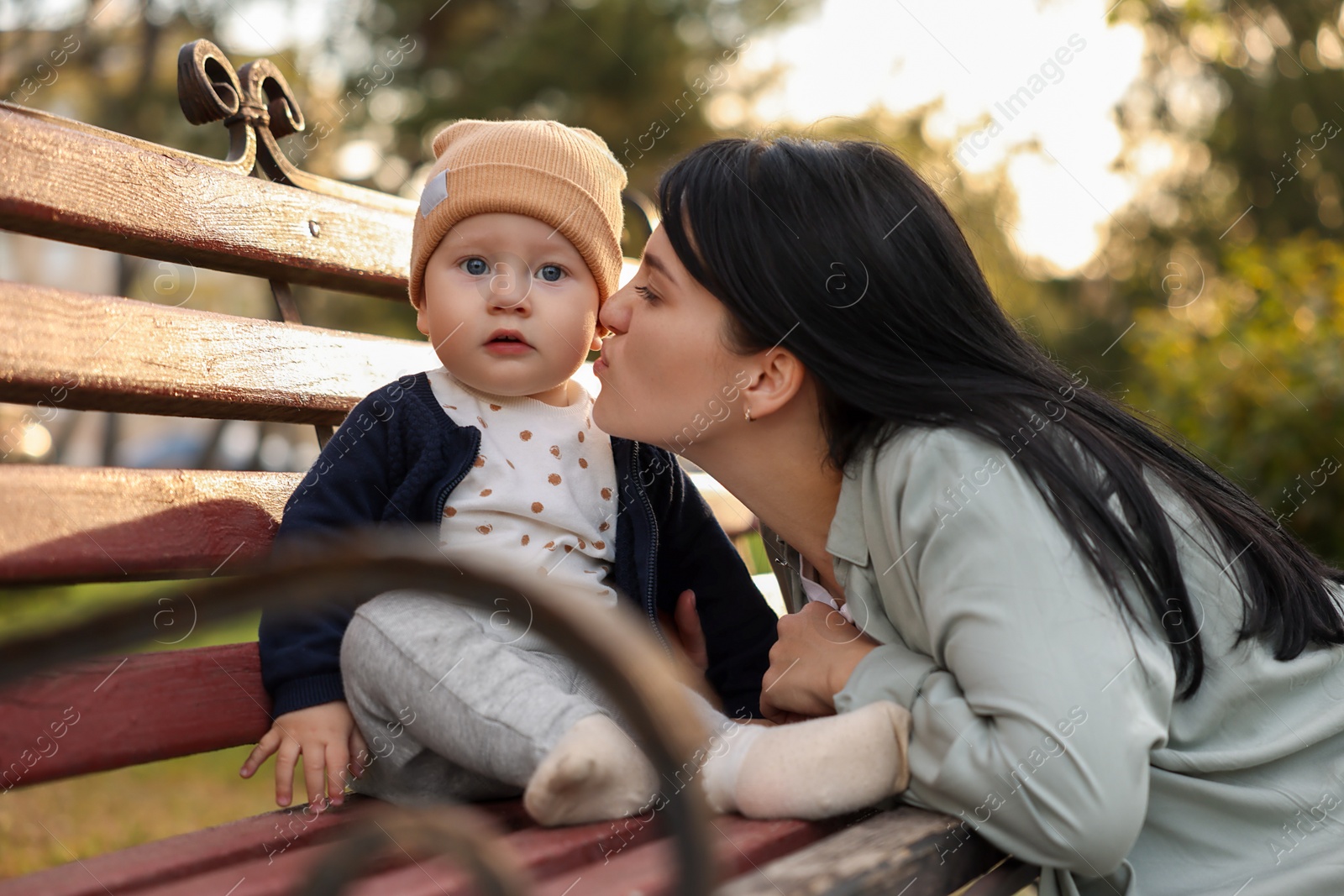 Photo of Mother kissing her baby on bench in park