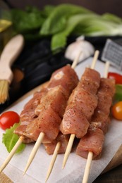 Skewers with cut raw marinated meat on wooden table, closeup