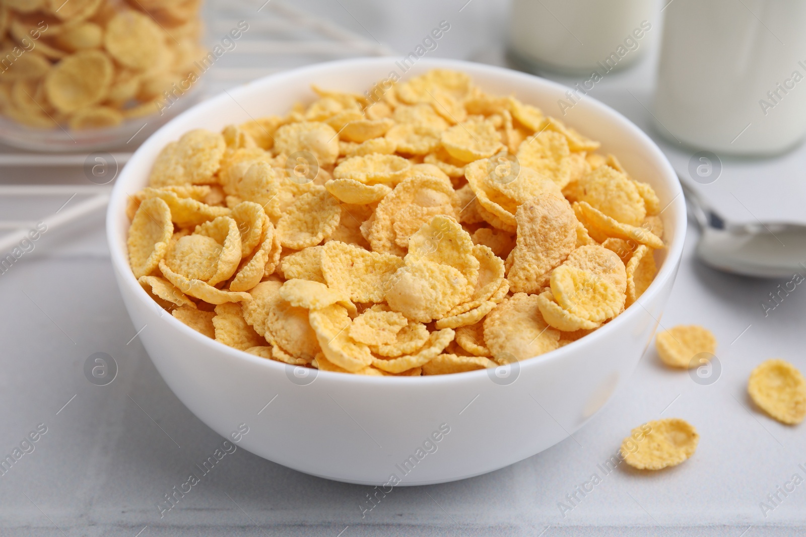 Photo of Tasty crispy corn flakes in bowl on white table, closeup. Breakfast cereal