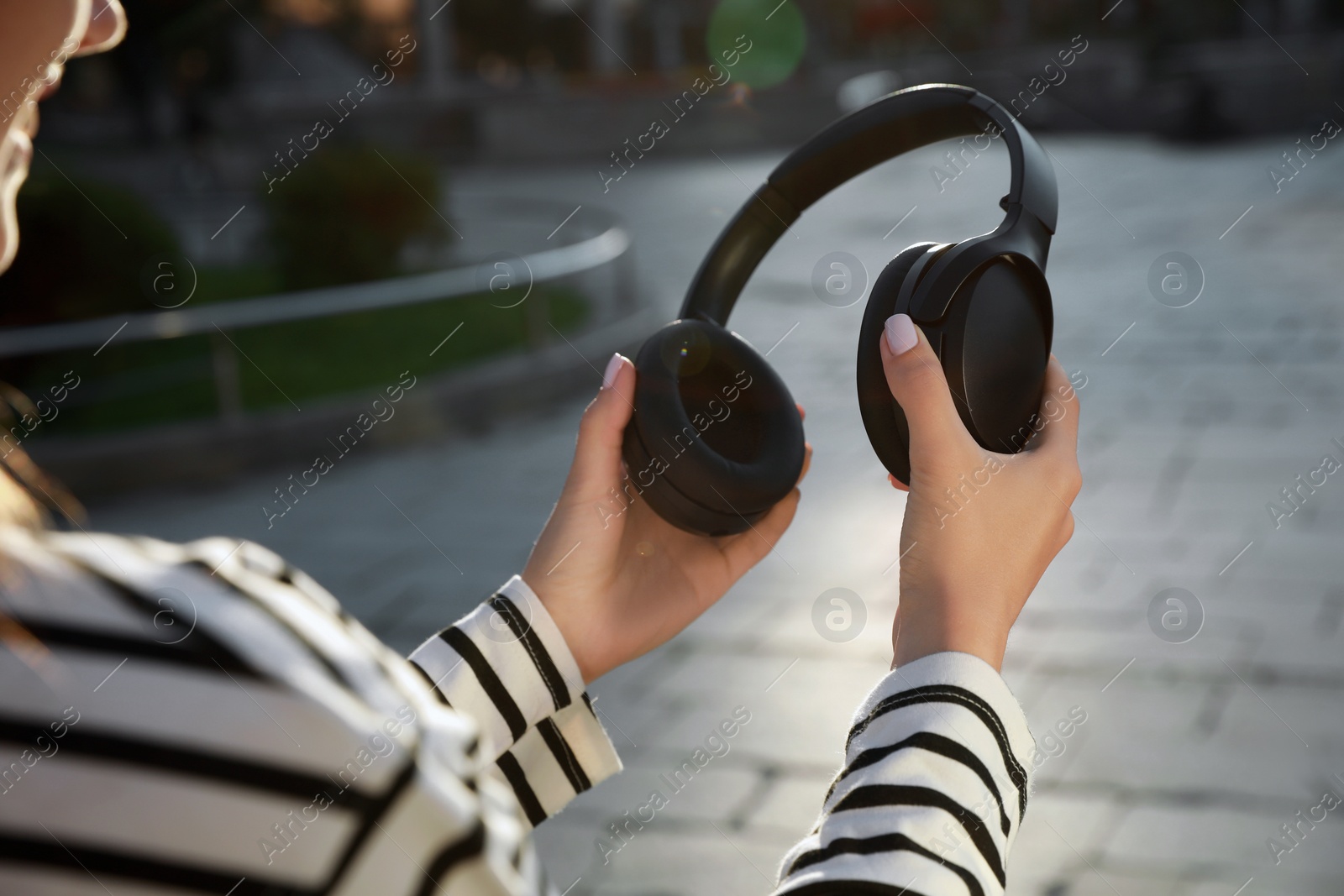 Photo of Woman holding black headphones on city street, closeup