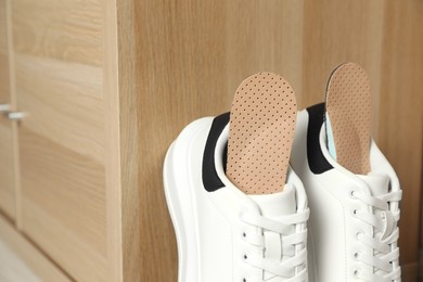 Photo of Orthopedic insoles in shoes near wooden drawer, closeup. Space for text