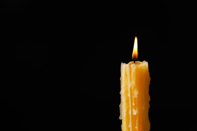 Photo of Burning church wax candle on black background, closeup. Space for text