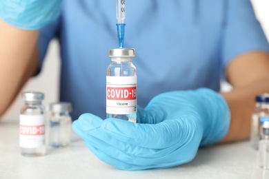 Photo of Doctor filling syringe with vaccine against Covid-19 at table, closeup