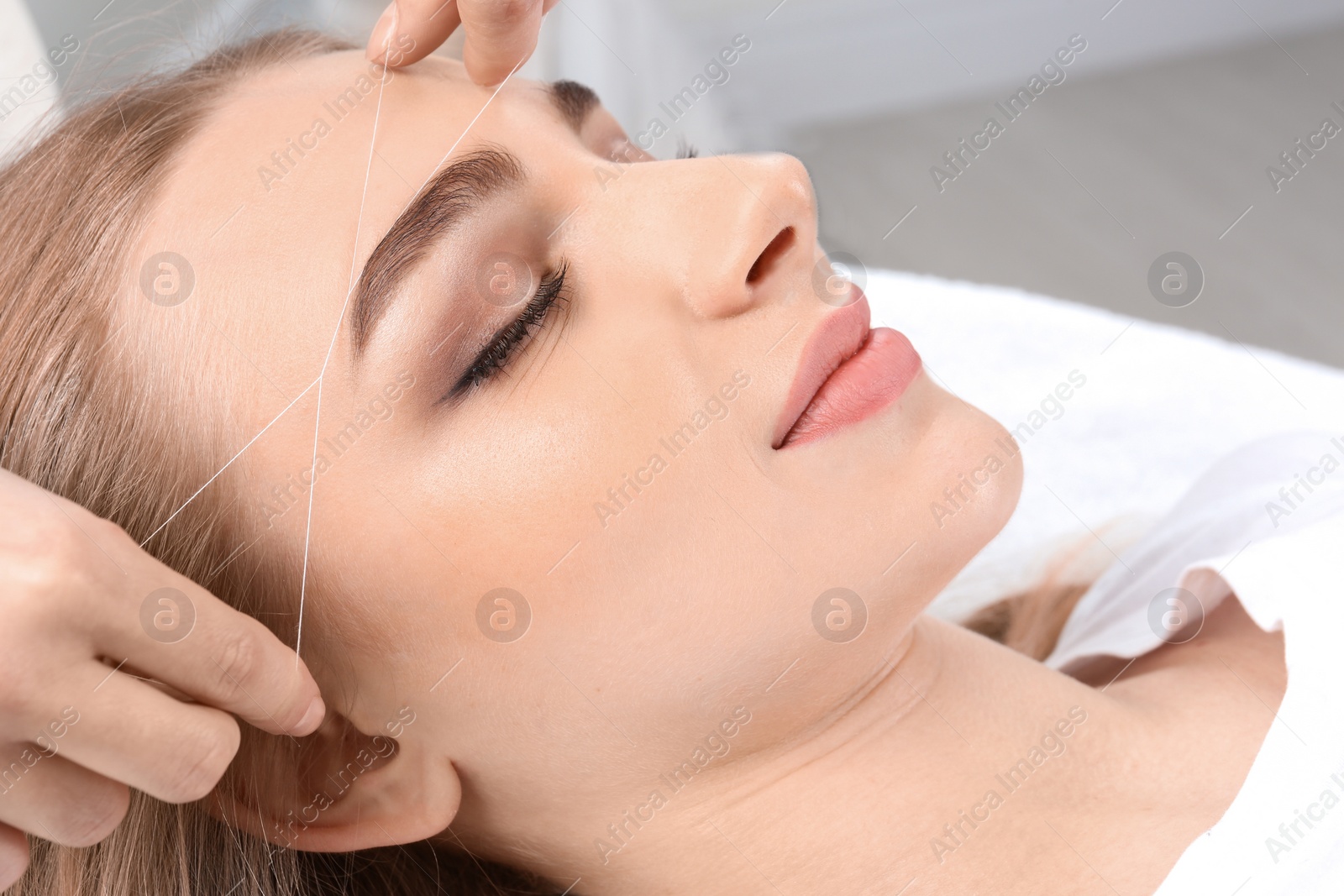 Photo of Young woman having professional eyebrow correction procedure in beauty salon