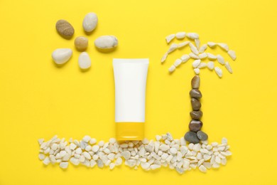 Photo of Suntan cream, sun and palm made of marble pebbles on yellow background, flat lay