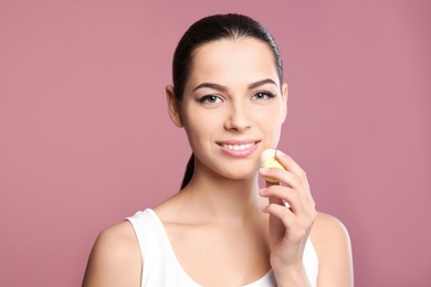 Young woman applying balm on her lips against color background