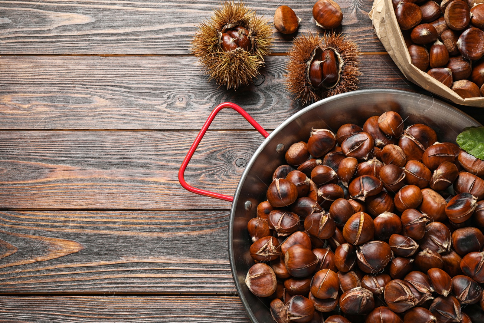 Photo of Delicious roasted edible chestnuts on brown wooden table, flat lay. Space for text