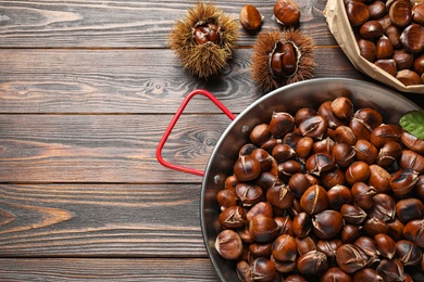 Delicious roasted edible chestnuts on brown wooden table, flat lay. Space for text