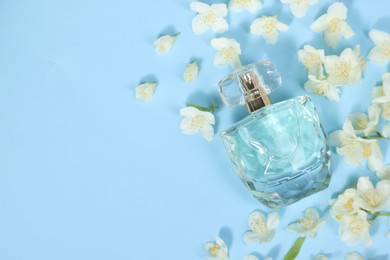 Aromatic perfume in bottle and beautiful jasmine flowers on light blue background, flat lay. Space for text