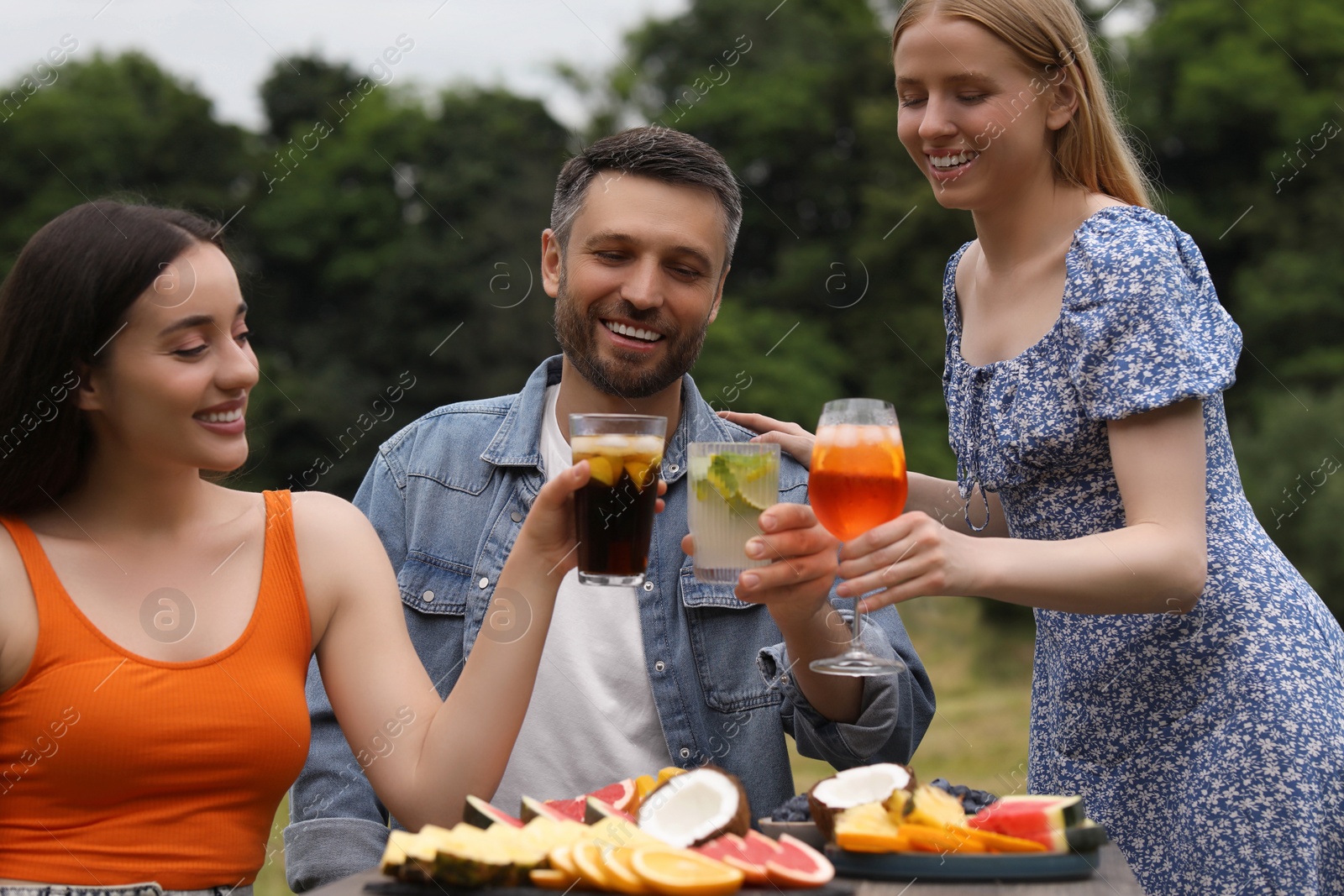 Photo of Happy friends clinking glasses with cocktails at table outdoors