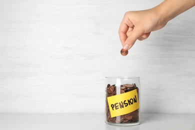 Photo of Woman putting coin in glass jar with label "PENSION" on table, closeup. Space for text