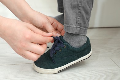 Mother helping son to tie shoe laces at home, closeup