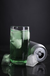 Photo of Tasty energy drink with ice cubes in glass and aluminium can on black table