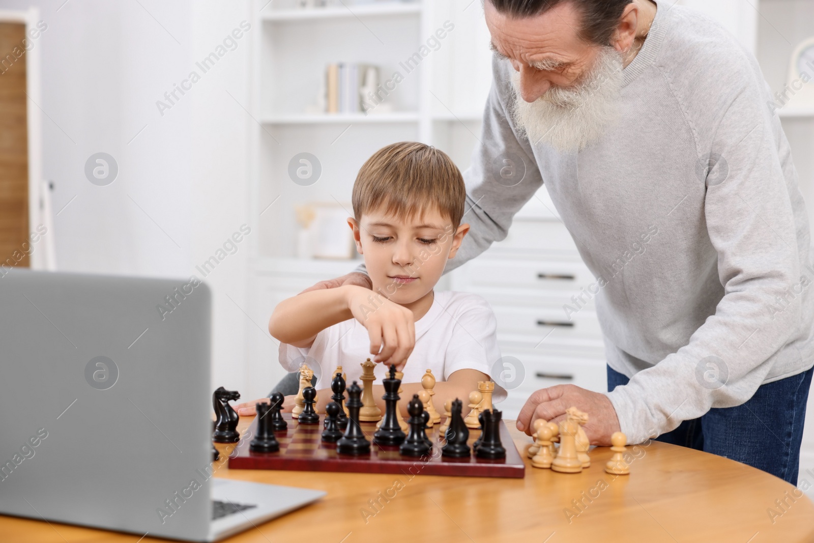 Photo of Grandfather teaching his grandson to play chess following online lesson at home