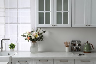 Bouquet of beautiful flowers on white countertop in kitchen